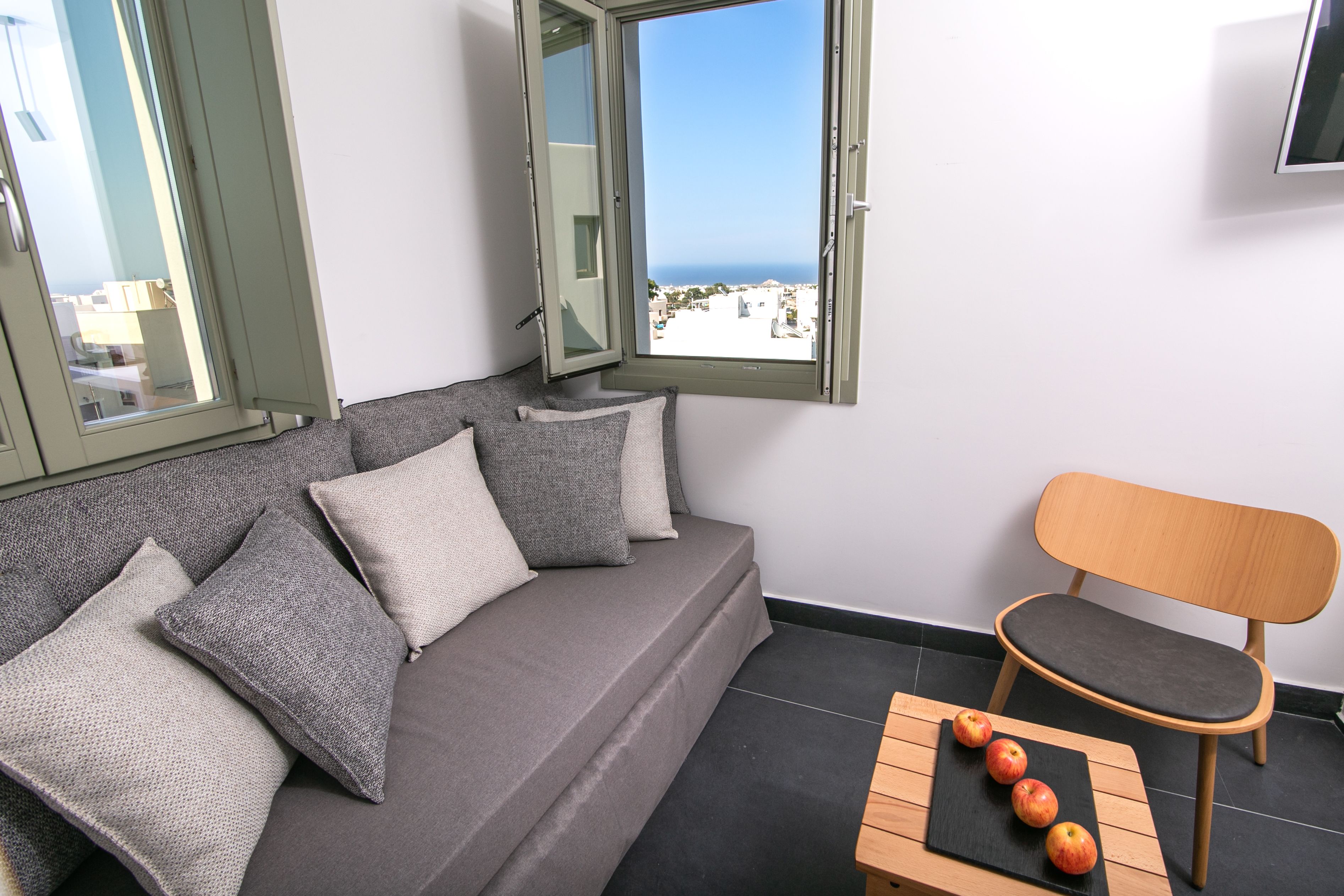 A modern room with a grey sofa, a wooden chair, and a table with apples.