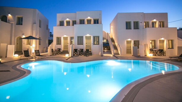 A swimming pool surrounded by modern white buildings with outdoor seating and staircases leading to upper floors. - Kallos Imar Boutique Hotel  (Santorini)