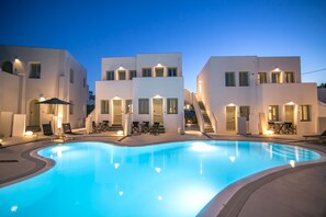 A swimming pool surrounded by modern white buildings with outdoor seating and staircases leading to upper floors. - Kallos Imar Boutique Hotel  (Santorini)