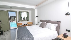 A modern bedroom with a large bed, a small table with a plant, and a view of a pool through an open door. - Kallos Imar Boutique Hotel  (Santorini)