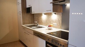 A modern kitchen with white cabinets, a stainless steel sink, a microwave, and a stove. - Ferienwohnung Muschel (Kopendorf auf Fehmarn)
