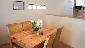 A wooden dining table with four chairs, a vase with flowers, and two candles. - Ferienwohnung Muschel (Kopendorf auf Fehmarn)
