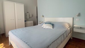Quarto com cama, ventoinha no teto, guarda-roupa e mesa de cabeceira.