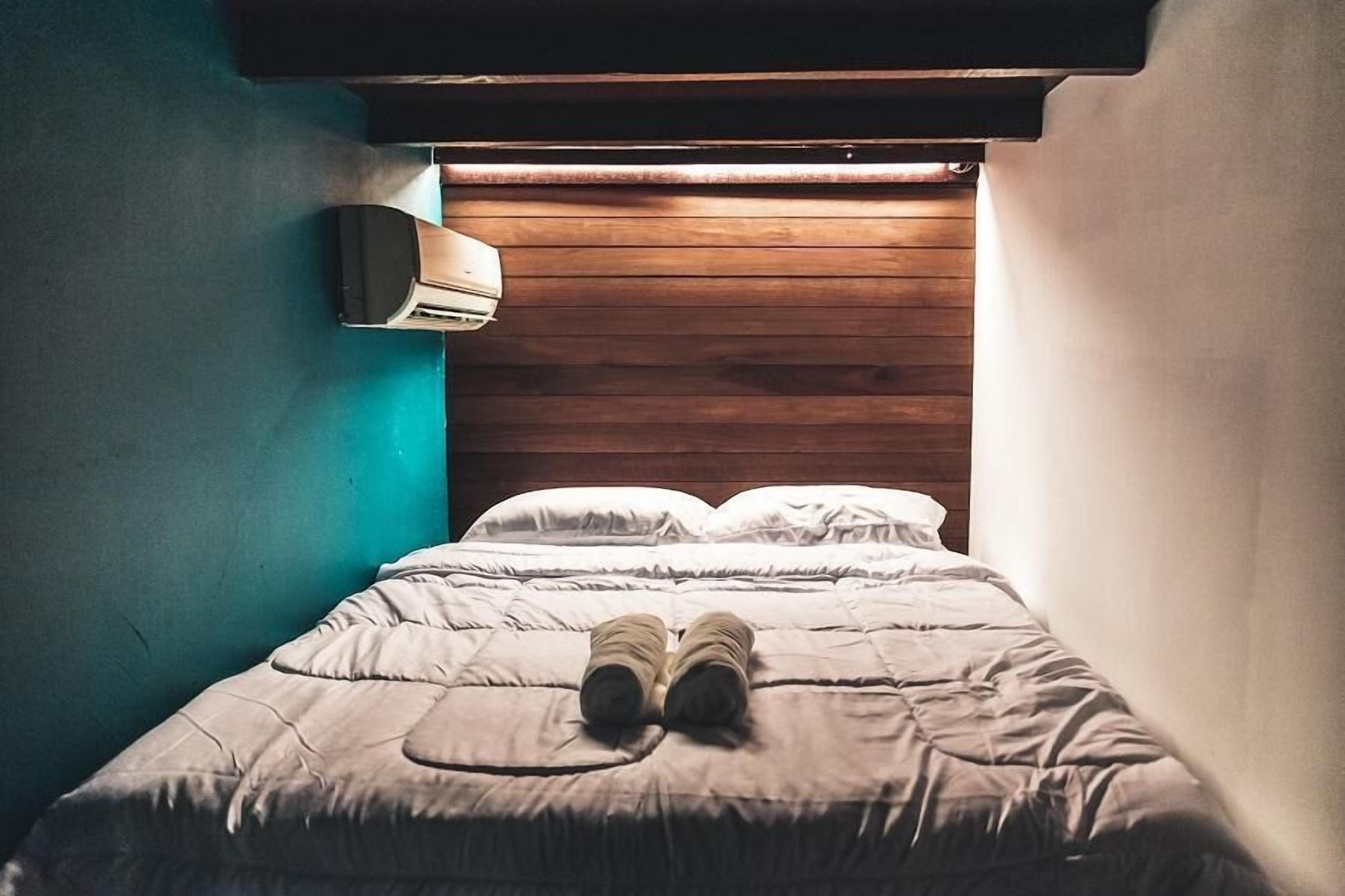 A bed with a wooden headboard, a wall-mounted air conditioner, and a single pillow.