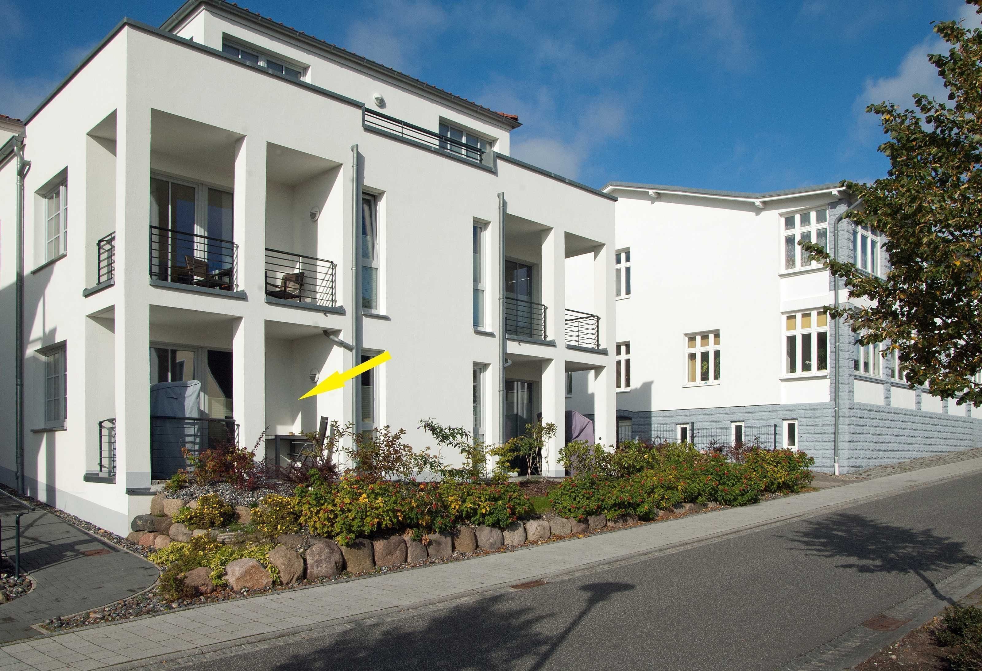 A modern two-story building with balconies, a paved driveway, and a landscaped garden area.