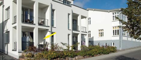 A modern two-story building with balconies, a paved driveway, and a landscaped garden area.