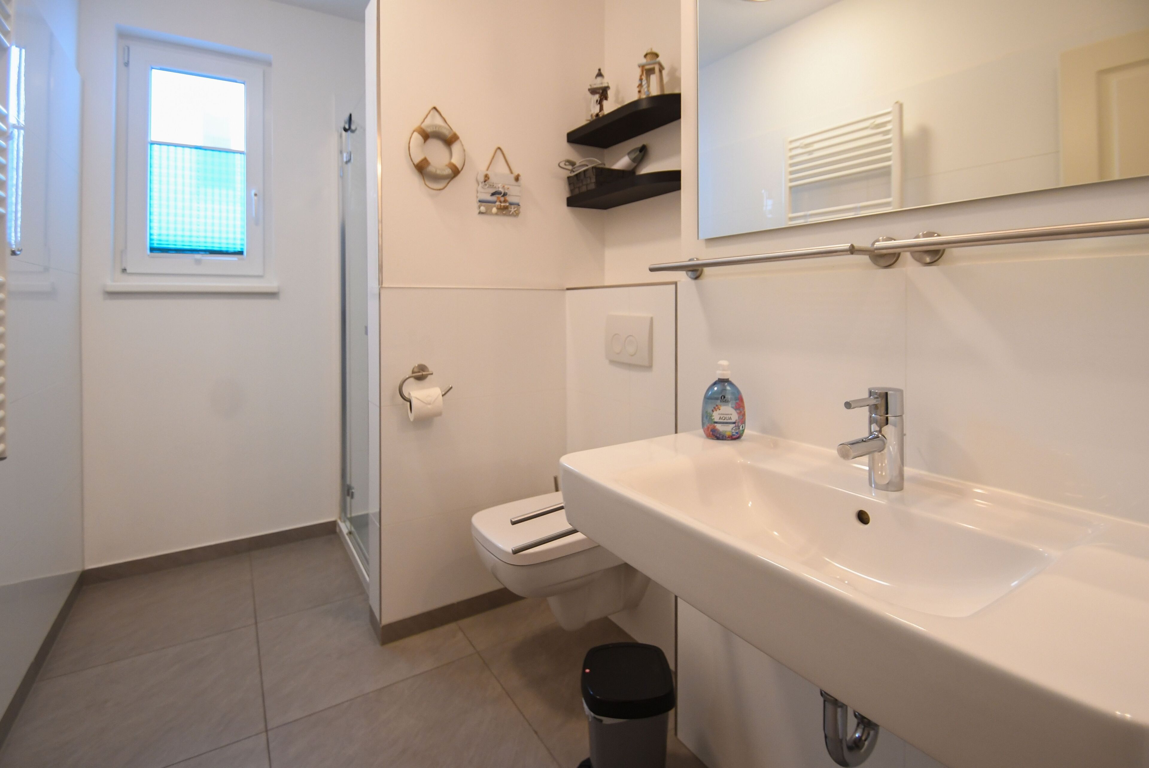 Une salle de bain moderne avec un lavabo blanc, des toilettes, une douche en verre et une fenêtre avec des stores.