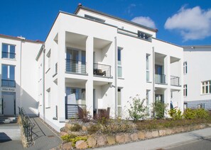 A modern multi-story residential building with balconies, a stone facade, and a clear sky.