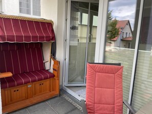 A cozy outdoor seating area with a wooden bench and a cushioned chair, adjacent to a sliding glass door leading to a patio.