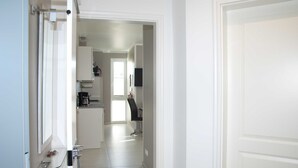 Un pasillo que conduce a una cocina con armarios blancos y una silla negra.