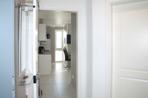 A hallway leading to a kitchen with white cabinets and a black chair.