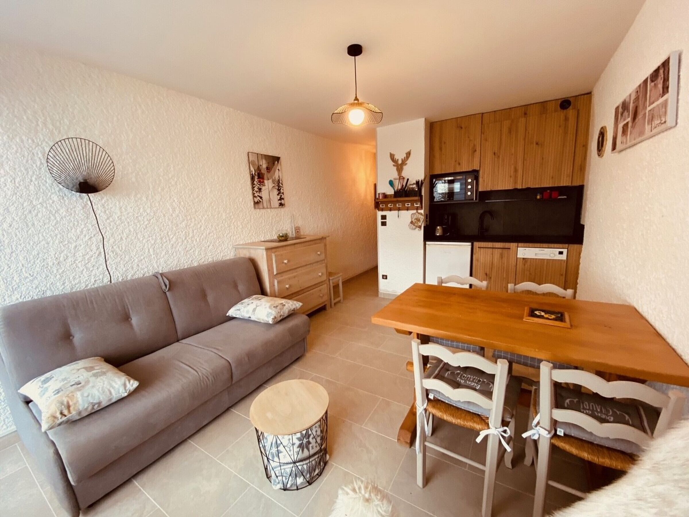 A compact living space with a sofa, a dining table with chairs, a small round table, a kitchenette, and a ceiling fan.