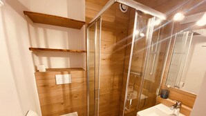 Un bagno moderno con finiture in legno, una doccia vetrata, un WC bianco e un lavabo con specchio sopra.