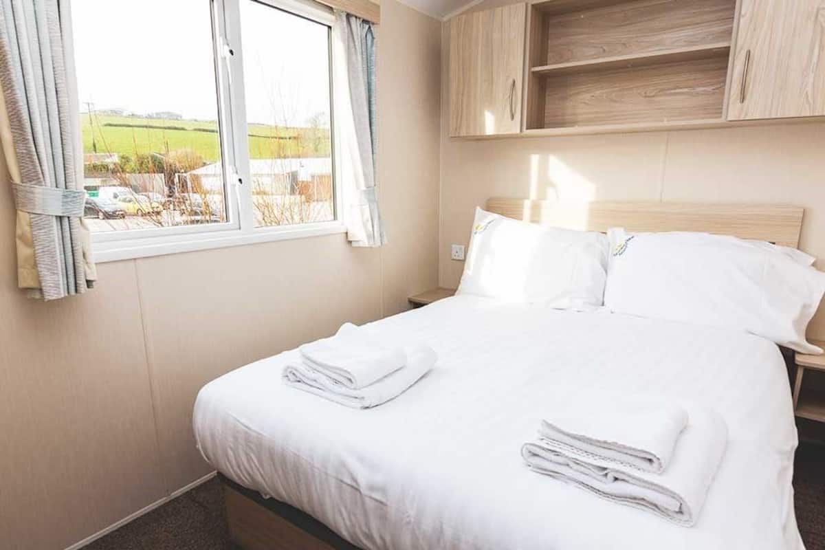 Un lit bien fait, avec du linge de lit et des serviettes blanches, une fenêtre avec des rideaux et des meubles en bois au-dessus du lit.