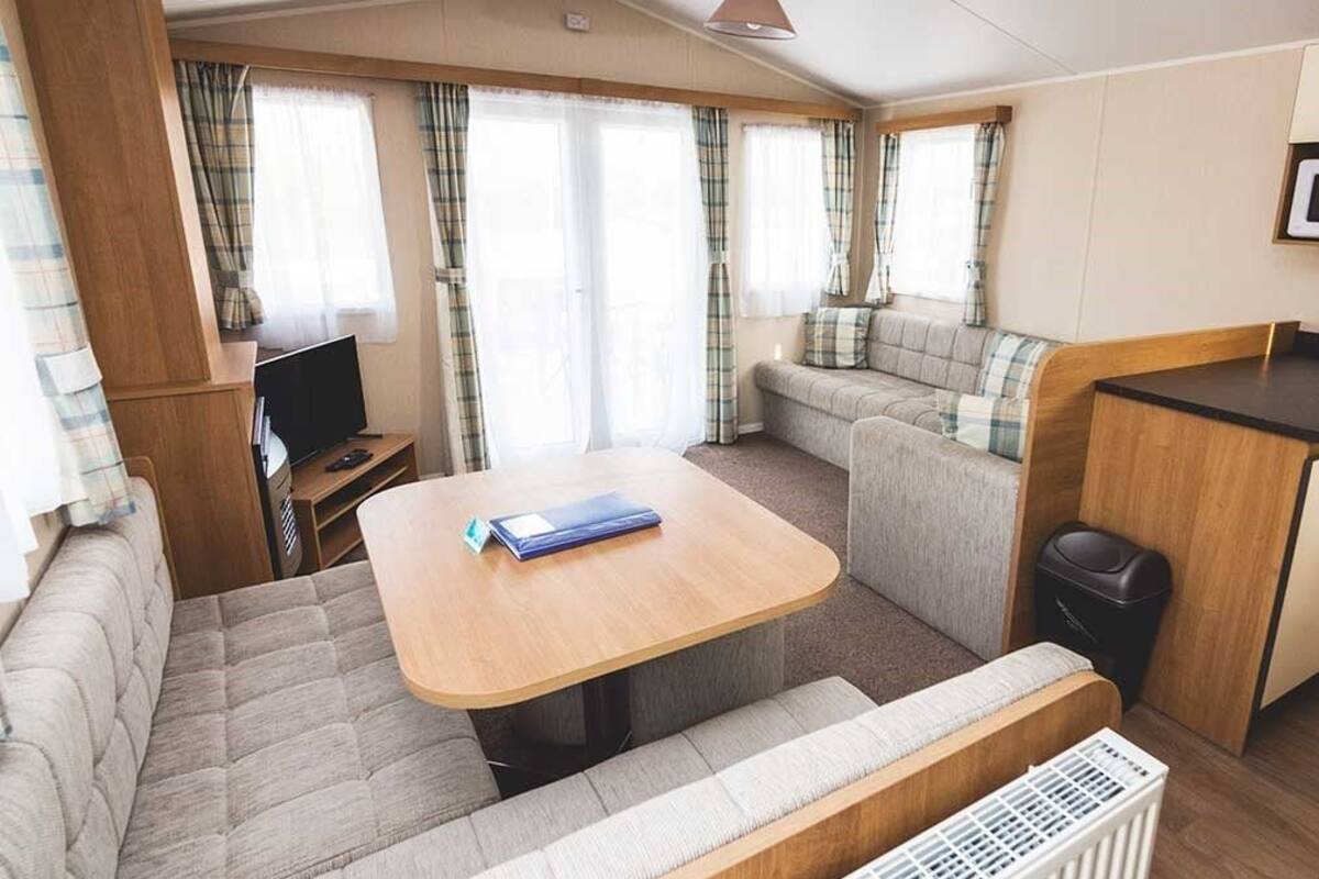 Un intérieur de camping-car compact comprenant un canapé, une petite table, un téléviseur et des rideaux.