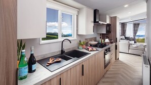 A modern kitchen with a large window, wooden cabinets, and a built-in oven. - Newquay Bay Holiday Resort (Newquay)