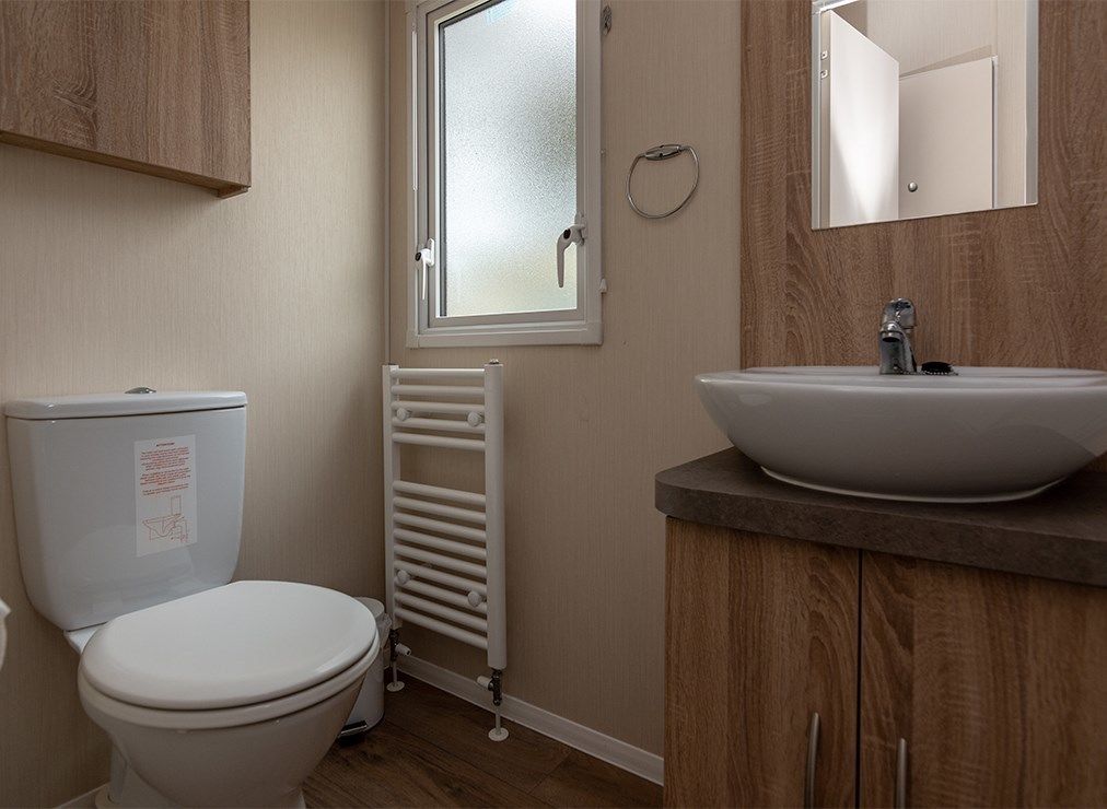 Een badkamer met een toilet, een wastafel, een spiegel en een raam.