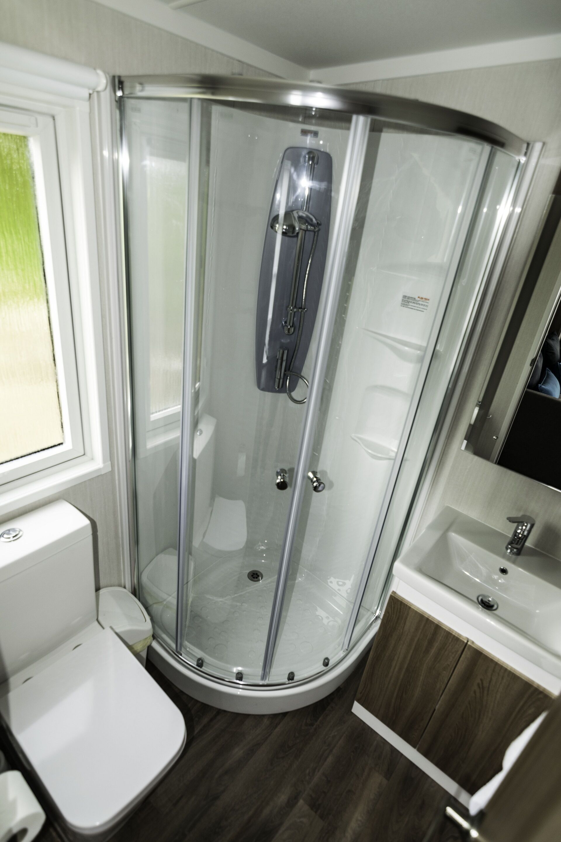Un baño moderno con cabina de ducha de vidrio, inodoro y lavamanos con espejo.