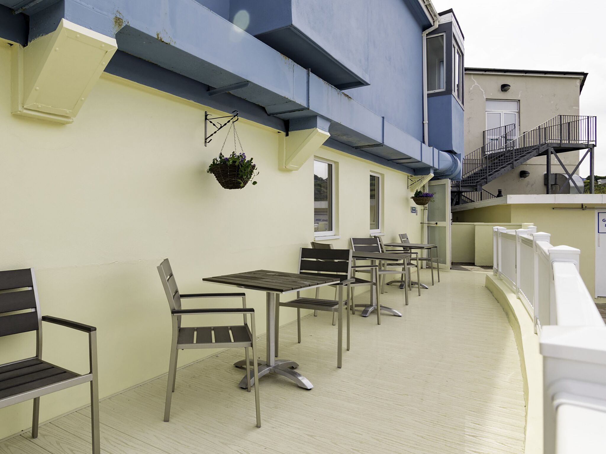 An outdoor seating area with tables and chairs, a hanging plant, and a staircase leading to an upper level.