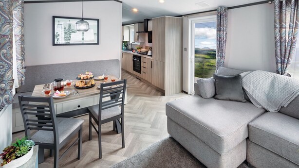 A modern living room with a grey sofa, a dining table with chairs, and a kitchen in the background. - Newquay Bay Holiday Resort (Newquay)