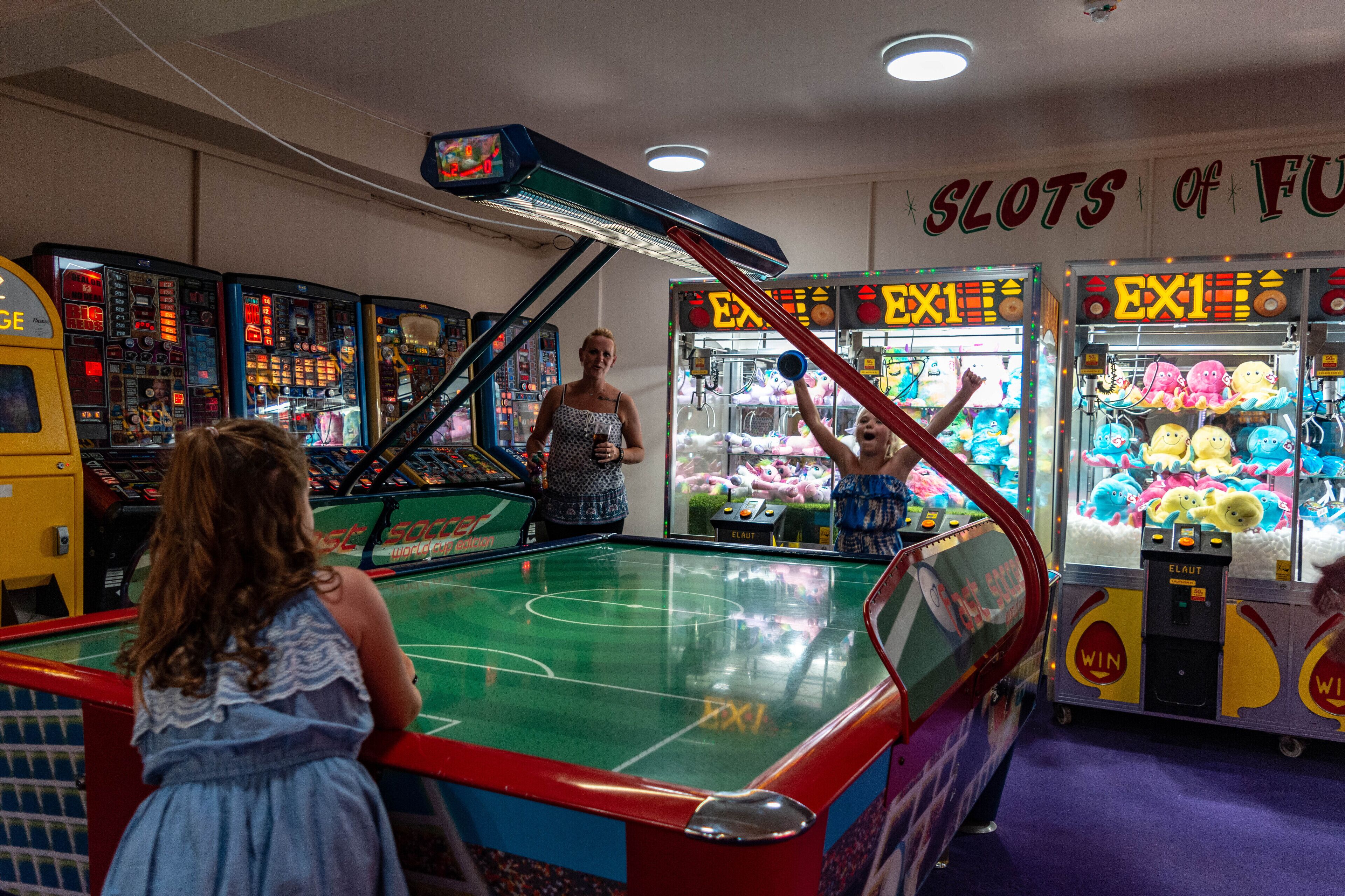 A pool table with a neon sign overhead, surrounded by claw machines and arcade games.