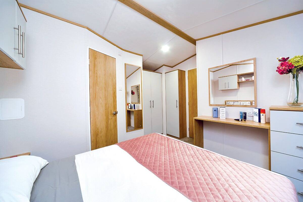 Une chambre à coucher avec un lit, une armoire, un miroir et un bureau agrémenté d’un vase de fleurs.