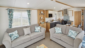 A compact living space with two sofas, a small wooden table, and a kitchenette. - Newquay Bay Holiday Resort (Newquay)