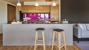 Une cuisine moderne avec des meubles en bois, un îlot central doté de tabourets, un éclairage suspendu et une vue sur l’espace de vie.