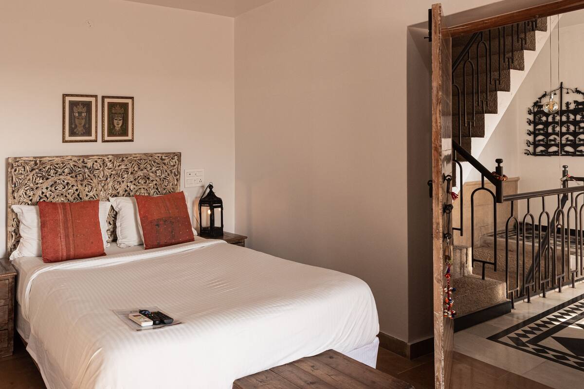 A bedroom with a large bed, a wooden bench, a nightstand, and a staircase with a railing.