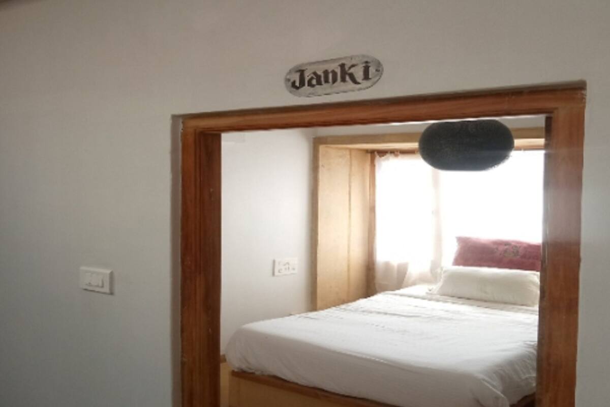 A bedroom with a bed, a wooden door frame, a light switch, and a sign above the door.