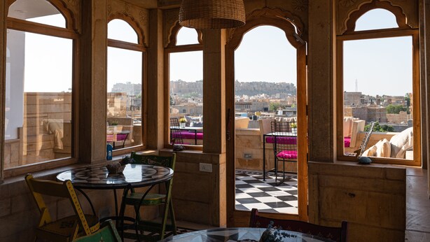 A room with a checkered floor, a round table, and a view of a cityscape through arched windows. - The Secret House - Adults Only (Jaisalmer)