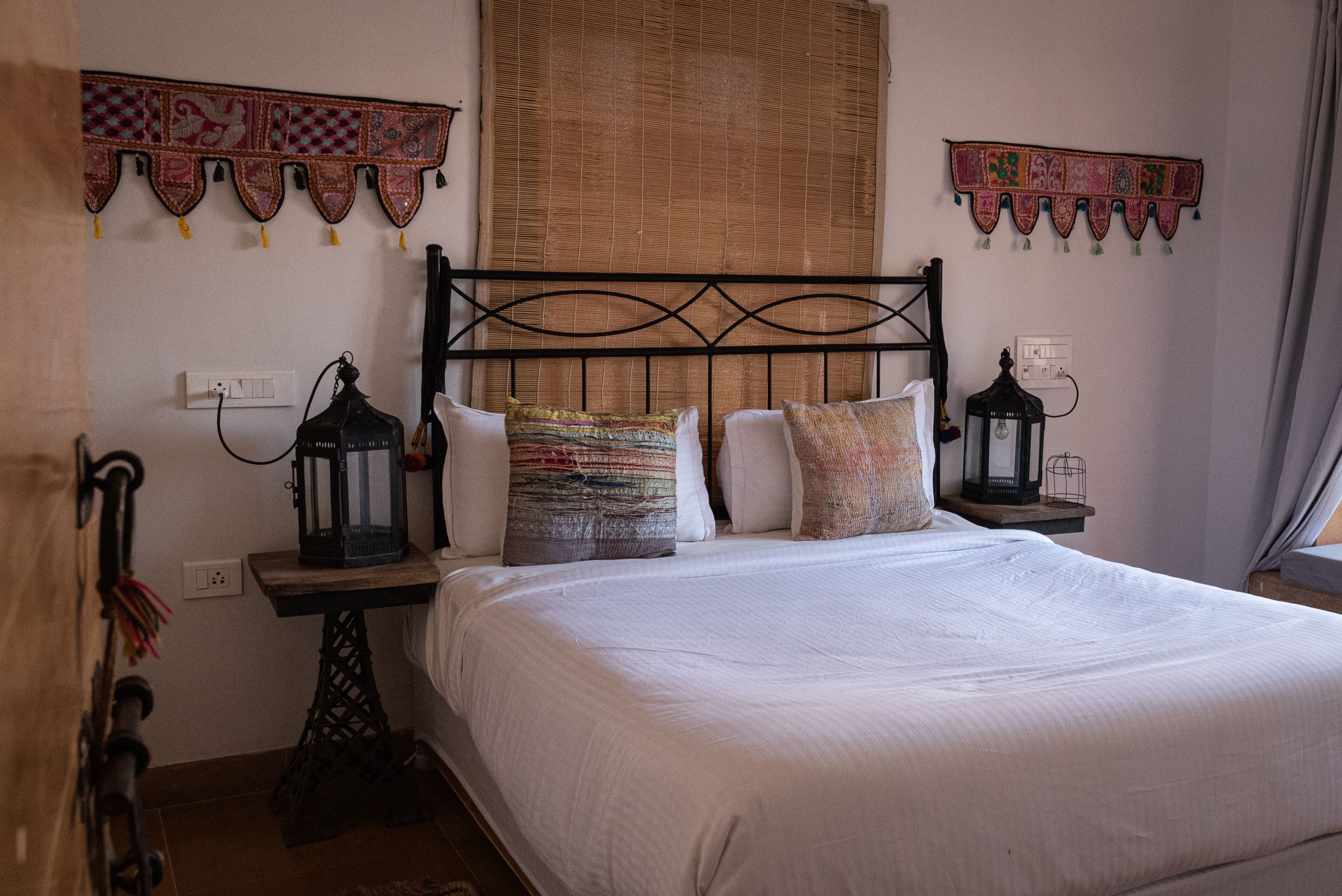 A bed with a black metal headboard, white bedding, and two wall-mounted lanterns.