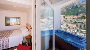 A bedroom with a bed, a small stool, a red pillow, a framed picture on the wall, and a balcony with a hot tub. - Villa Anfitrite (Positano)