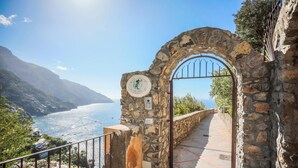 A stone archway leading to a coastal path with a view of the sea and mountains. - Villa Anfitrite (Positano)
