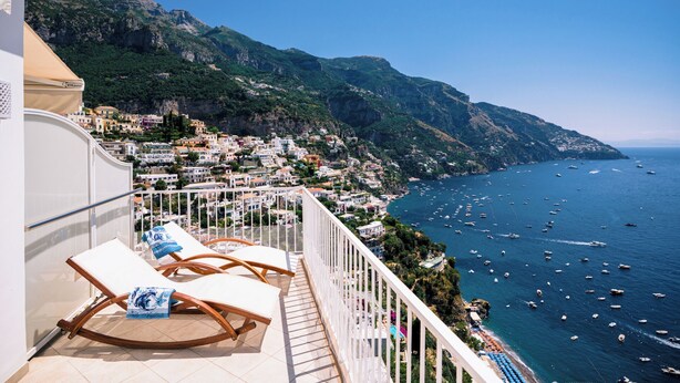 A balcony with lounge chairs overlooking a coastal town and the sea. - Villa Anfitrite (Positano)
