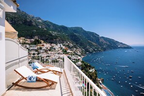 A balcony with lounge chairs overlooking a coastal town and the sea. - Villa Anfitrite (Positano)