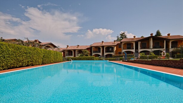 A rectangular swimming pool with clear blue water, surrounded by a tiled deck. - Appartamento Arianna (Manerba del Garda)