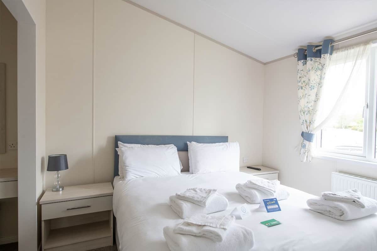 A hotel room with a bed, a nightstand, a lamp, and towels on the bed.