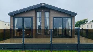 A modern mobile home with a flat roof, large windows, and a deck area.