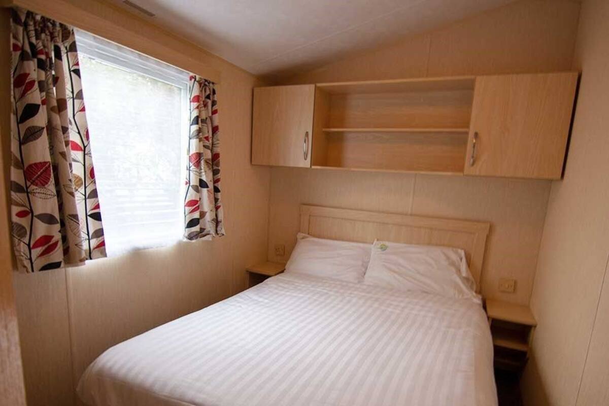 A bedroom with a bed, a window with curtains, and built-in wooden cabinets above the bed.