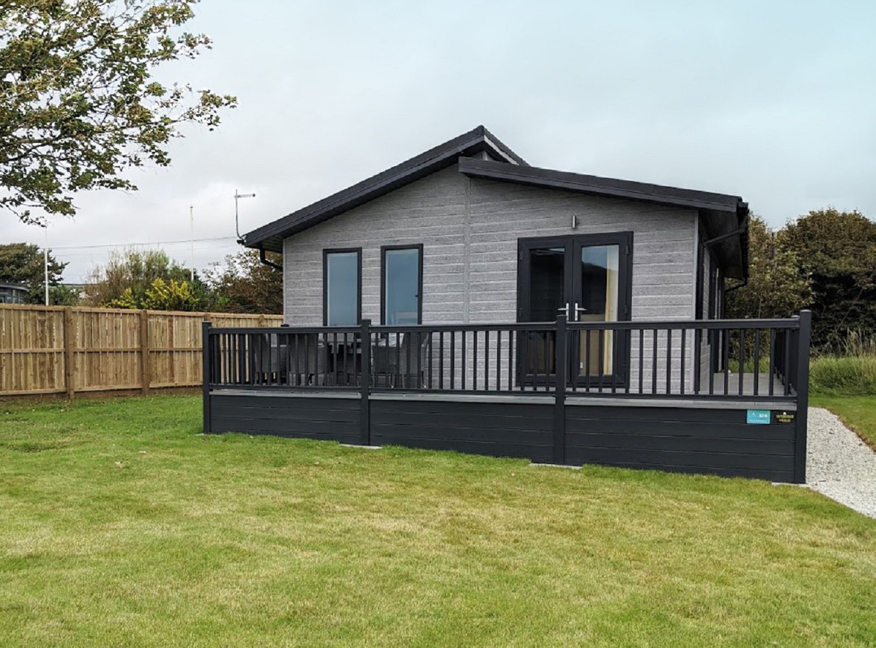 A modern two-story house with a flat roof, a balcony, and a fenced yard.