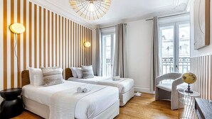 A hotel room with two beds, a wooden floor, a large window, and a balcony.