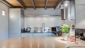 A modern kitchen with a wooden dining table, stainless steel appliances, and a hanging light fixture. - Trastevere Luxury Loft, unique, modern and with an Italian art gallery (Roma)