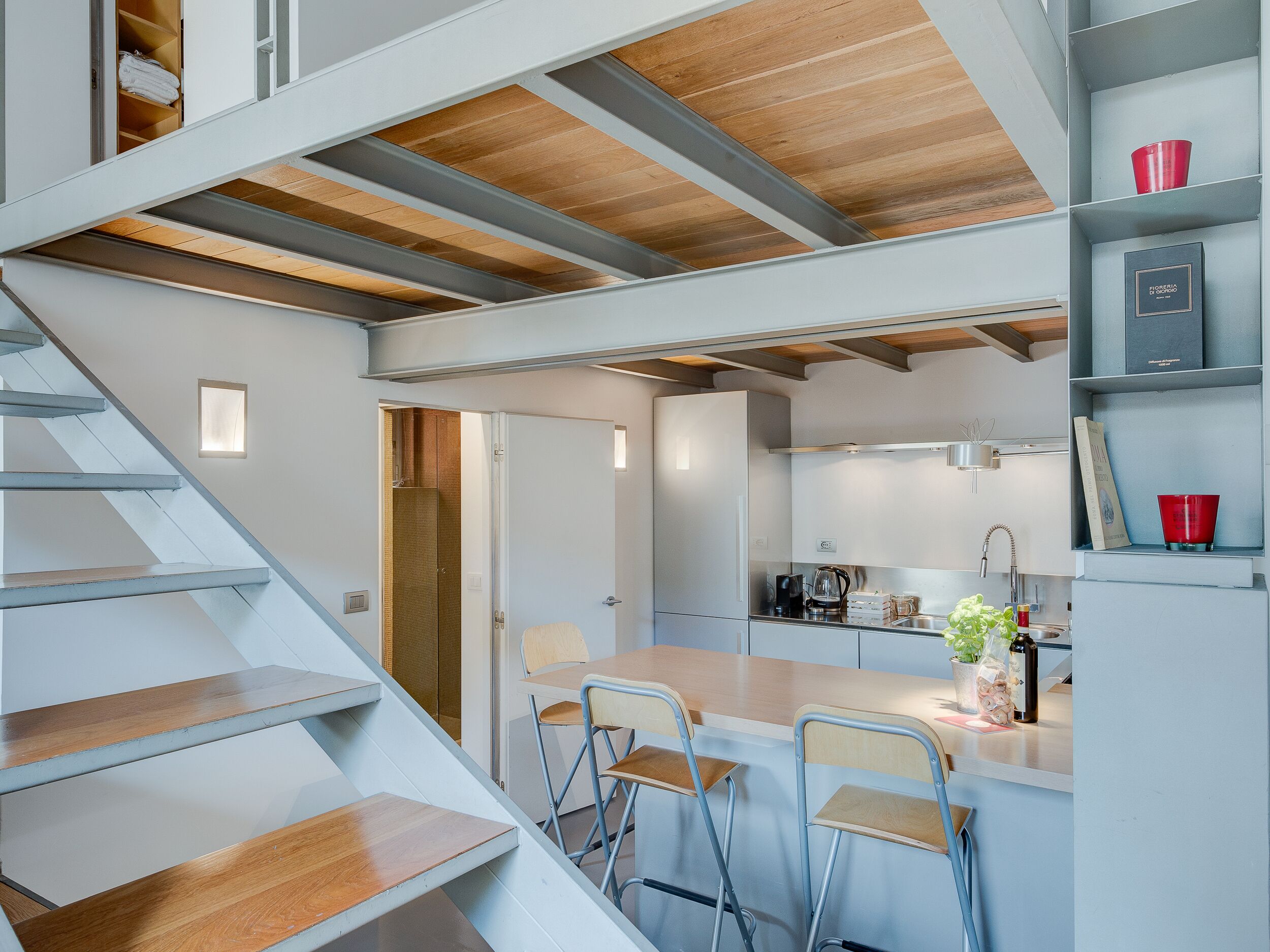 A modern kitchen with a wooden staircase, a dining area with bar stools, and a kitchen counter with various items.