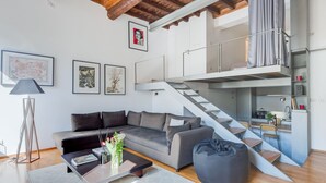 A modern living space with a grey sofa, a coffee table, and a staircase leading to a loft area. - Trastevere Luxury Loft, unique, modern and with an Italian art gallery (Roma)