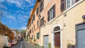A narrow cobblestone street lined with traditional buildings, featuring a mix of closed and open shops, and parked vehicles on one side. - Trastevere Luxury Loft, unique, modern and with an Italian art gallery (Roma)