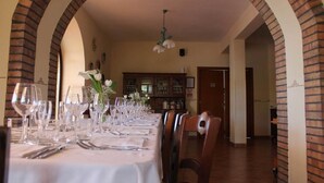 Un espace repas avec une longue table dressée pour le repas, flanqué d’arches en briques et surmonté d’un luminaire suspendu.