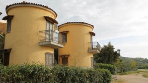 Un bâtiment jaune doté de deux balcons, entouré de verdure et bordé d’un chemin de terre.