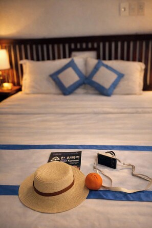 A bed with a striped headboard, two pillows with blue diamond patterns, a straw hat, an orange, and a black camera on a blue cloth.