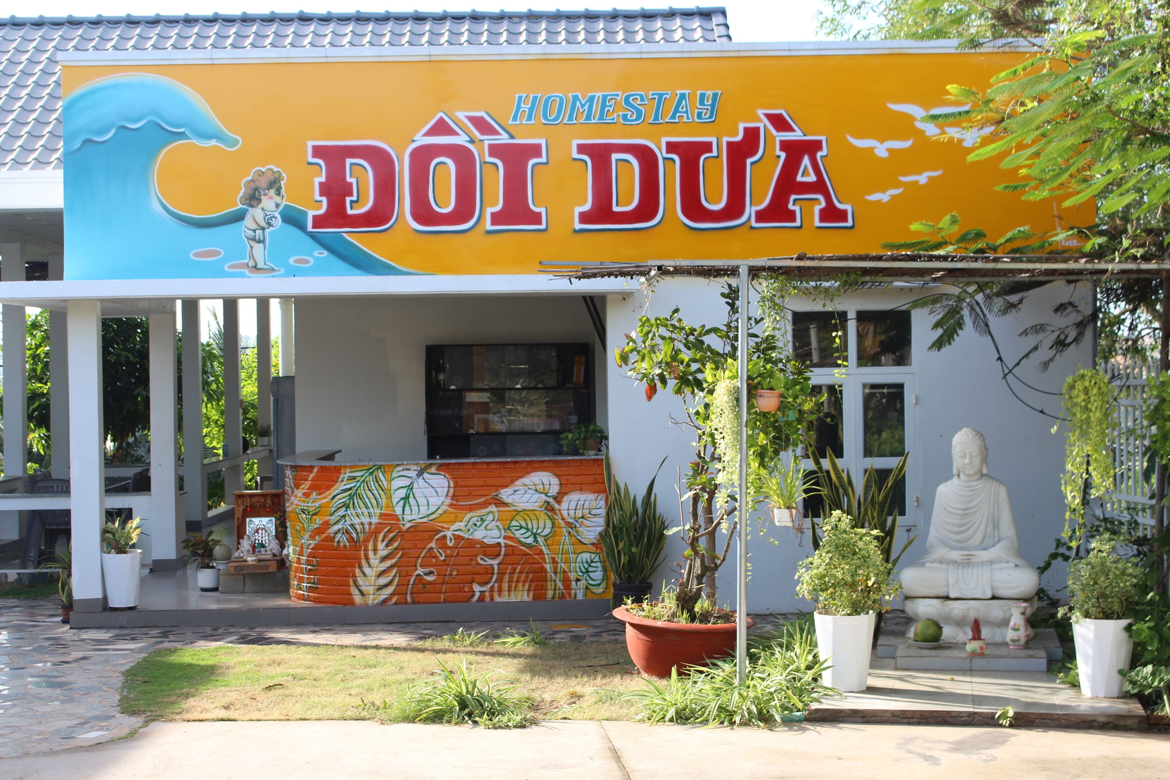Ein Gebäude mit einer großen Beschilderung mit der Aufschrift "Homestay Doi Dua" und einer Buddha-Statue davor.